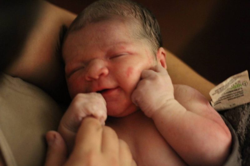 Newborn baby being held by the mom. Baby is holding moms finger. 