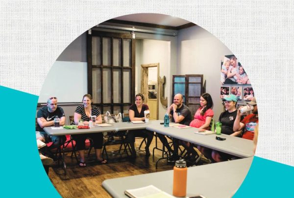 Text: Birth Boot Camp: More Than a Method. Image: Room full of pregnant couples all sitting around a classroom style table taking a childbirth class.